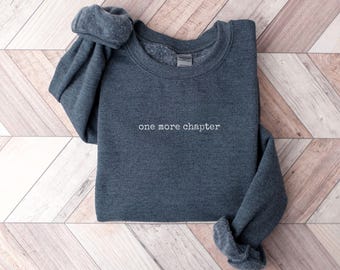 May include: A dark gray sweatshirt with the text "one more chapter" embroidered in white on the front.