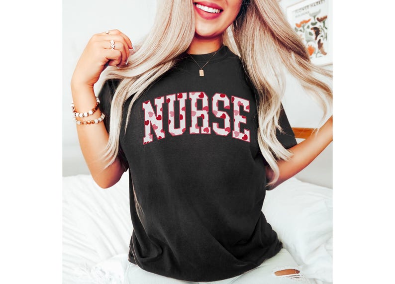 Pode incluir: Uma camiseta preta com um contorno branco da palavra "NURSE" em cora&ccedil;&otilde;es vermelhos e rosa.