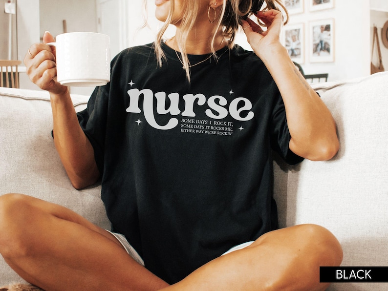 Pode incluir: T-shirt preta com a palavra "nurse" em fonte retr&ocirc; branca, com o texto "SOME DAYS I ROCK IT, SOME DAYS IT ROCKS ME, EITHER WAY WE'RE ROCKIN" abaixo. A camisa &eacute; de estilo casual.