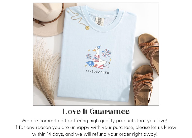 Op de afbeelding: Lichtblauw T-shirt met een cartoonillustratie van een gans die een feestmuts draagt en op een vuurwerk rijdt. De tekst "FIREQUACKER" is onder de illustratie gedrukt. Het T-shirt ligt op een wit oppervlak met een strohoed en sandalen.