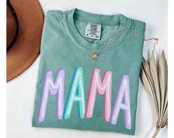 May include: A green t-shirt with the word "MAMA" printed in rainbow colors. The shirt is made of a soft, comfortable material and has a relaxed fit.