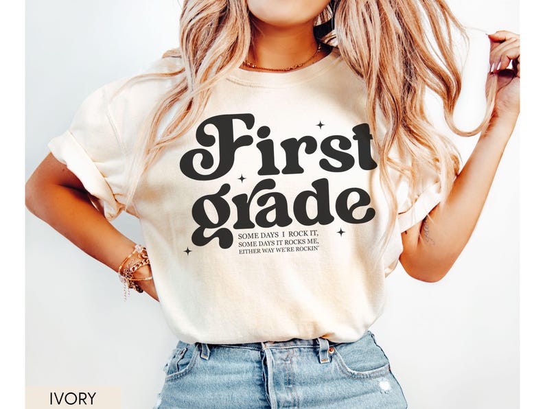 Puede incluir: Camiseta de color marfil con las palabras "First Grade" en una fuente retro audaz. La camiseta tambi&eacute;n presenta el texto "SOME DAYS I ROCK IT, SOME DAYS IT ROCKS ME, EITHER WAY WE'RE ROCKIN". Una camiseta elegante y c&oacute;moda para el primer grado.