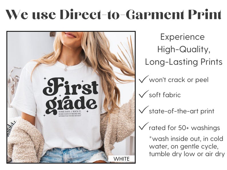 Puede incluir: Camiseta blanca con la frase "First Grade" en una fuente retro. La camiseta tambi&eacute;n tiene el texto "SOME DAYS I ROCK IT, SOME DAYS IT ROCKS ME, EITHER WAY WE ROCK IT." La imagen muestra una impresi&oacute;n directa sobre la prenda.