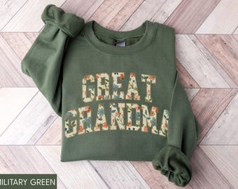 May include: Military green sweatshirt with the words "GREAT GRANDMA" in a floral pattern. The sweatshirt has a crew neck and long sleeves with ribbed cuffs. The text "MILITARY GREEN" is at the bottom.