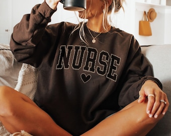 May include: A brown sweatshirt with the word "NURSE" in black letters with a small heart below it.
