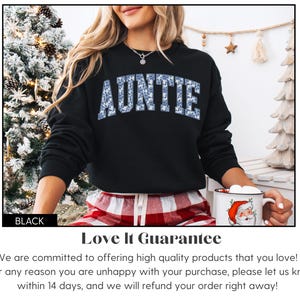 Peut inclure: Sweat-shirt noir avec le mot "AUNTIE" en motif floral bleu. L'image pr&eacute;sente un th&egrave;me de vacances. Une tasse blanche avec un motif de P&egrave;re No&euml;l est &eacute;galement visible.