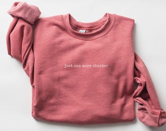 May include: A pink sweatshirt with the text "Just one more chapter" in white.