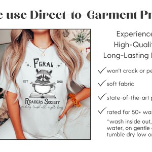 May include: White t-shirt with a black and white illustration of a raccoon reading a book. The text on the shirt reads "Feral Readers Society" and "reading trash all night long".