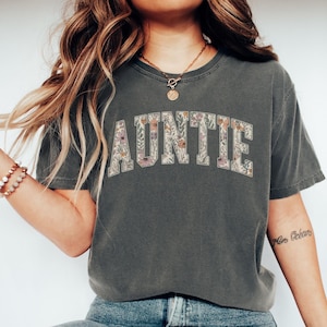 May include: A gray t-shirt with a floral print of the word "AUNTIE" in white letters.