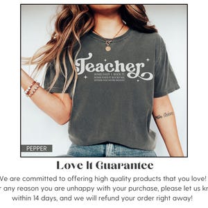 May include: Dark grey t-shirt with the word "Teacher" in a white, stylized font. The shirt also features the text "Some days I rock it, some days it rocks me, either way you're rocked!" A casual, comfortable tee.