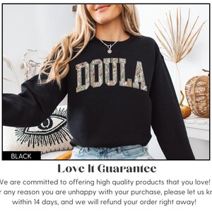 May include: Black sweatshirt with the word "DOULA" in floral print lettering. The sweatshirt is a crew neck style. The word "BLACK" is in a black rectangle at the bottom left of the image.