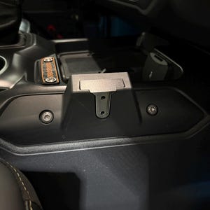 May include: Black plastic car console with a hinged lid and two visible screws. A USB port is visible on the right side. The console is part of a vehicle's interior.