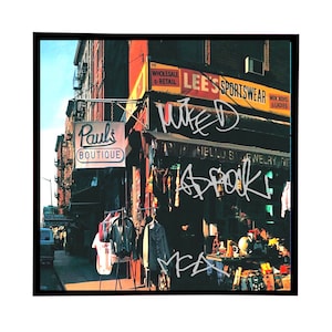 May include: A vintage photograph of a storefront in New York City. The storefront has a sign that reads "Paul's Boutique". There is a sign above the storefront that reads "Lee's Sportswear". The storefront is decorated with colorful clothing and other items. The image is signed "M.C.A.  Wiped A Spook"