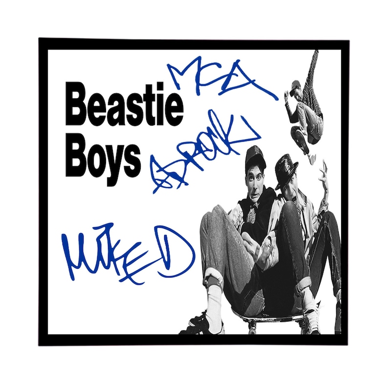 May include: Black and white photo of three men, two sitting on a skateboard and one standing in the air. The men are wearing casual clothing and the photo is signed "Beastie Boys" in black and "M.E.A.  " and "MIKE D" in blue.