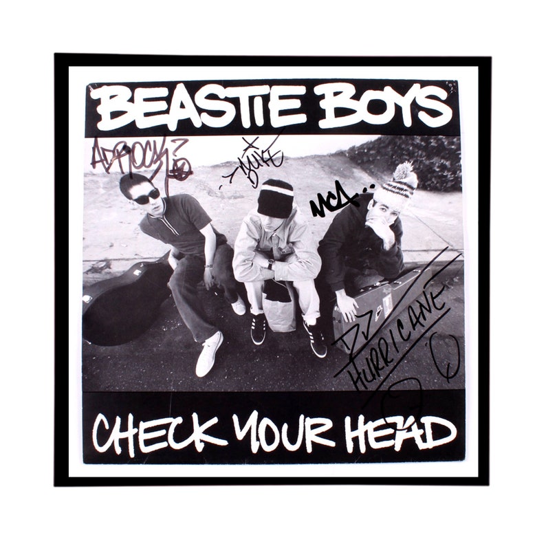 May include: A black and white photo of three men, signed by the band Beastie Boys. The photo is framed in black and the album title "Check Your Head" is printed below the photo.