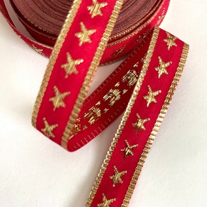 Puede incluir: Cinta roja con estrellas doradas y ribete dorado. La cinta est&aacute; enrollada y los extremos cuelgan.