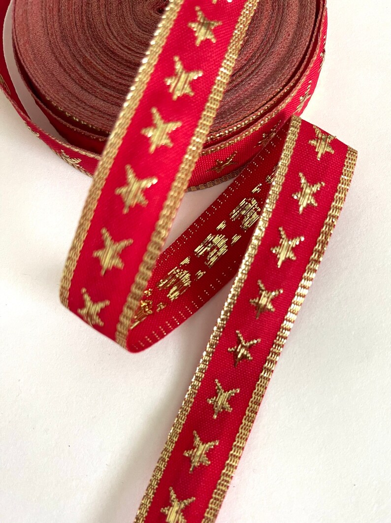 Puede incluir: Cinta roja con estrellas doradas y ribete dorado. La cinta est&aacute; enrollada y los extremos cuelgan.