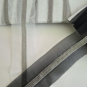 May include: Close-up of decorative trim featuring silver beads on white and black mesh fabric. The trim is arranged in vertical stripes on the white fabric and a single strip on the black fabric. The mesh has a hexagonal pattern.