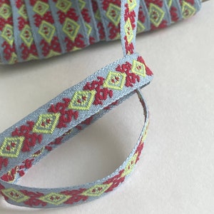 May include: A close-up of a blue, red, and yellow patterned ribbon. The ribbon is woven with a geometric design.