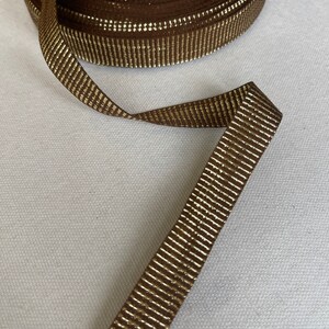 May include: Brown ribbon with gold metallic stripes. The ribbon is rolled up and a length is extended.