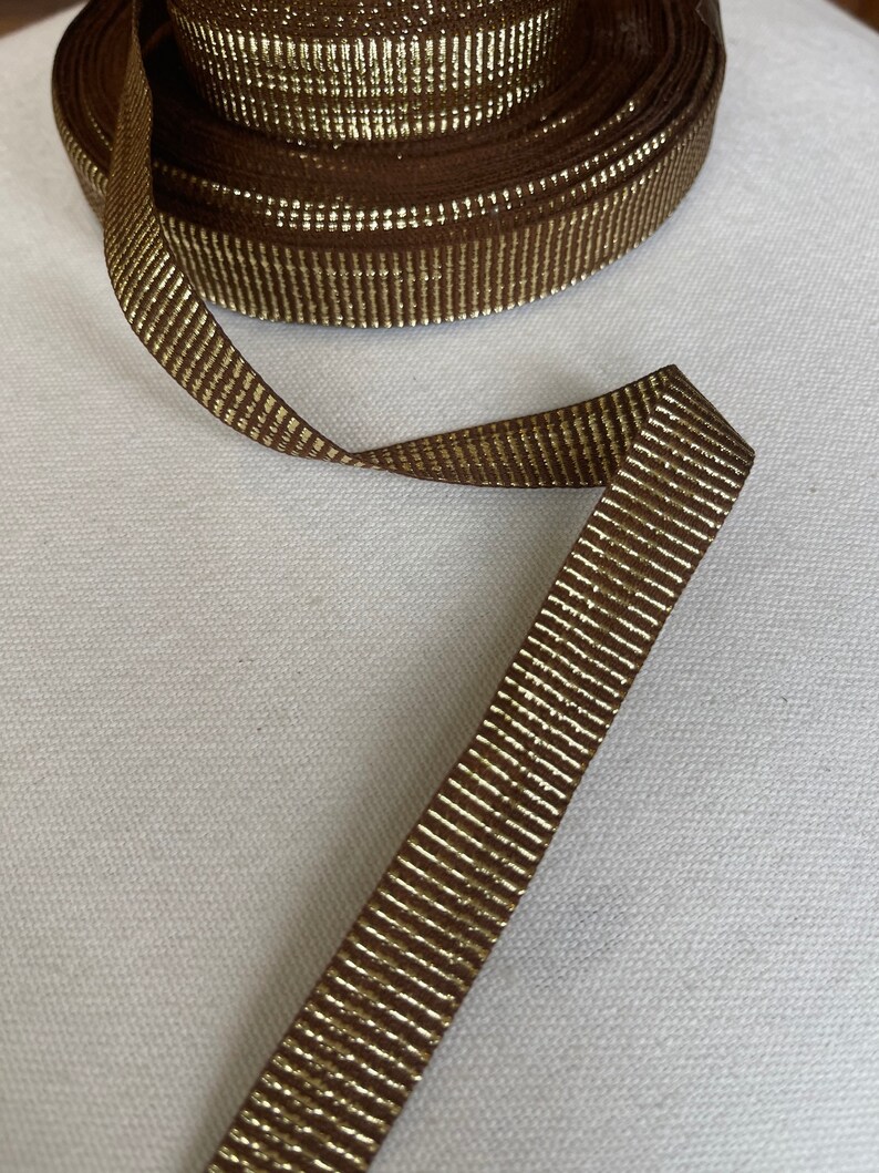 May include: Brown ribbon with gold metallic stripes. The ribbon is rolled up and a length is extended.