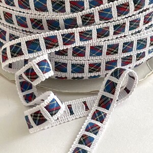 May include: White trim with a red, blue, and yellow plaid pattern. The trim is folded and shows the pattern on both sides.