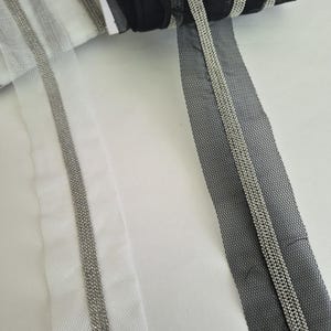 May include: Rolls of black and white tulle ribbon with silver beaded trim. The ribbon is displayed on a white surface. The tulle has a mesh-like appearance, and the silver trim adds a decorative element to the ribbon.