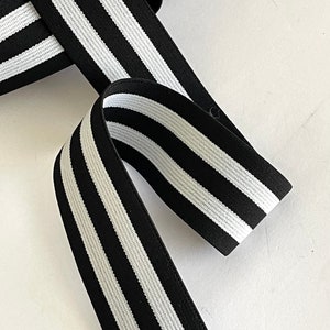 May include: Black and white striped elastic with a textured surface. The elastic is folded and arranged in a diagonal pattern.