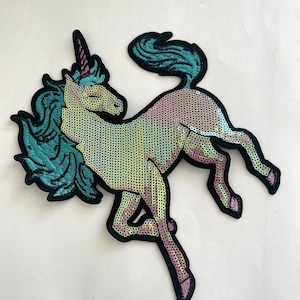 May include: A sparkly iridescent unicorn patch with a teal mane and tail. The unicorn is outlined in black and has a pink horn.