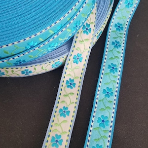 May include: Two rolls of blue and white ribbon with a floral pattern. The ribbon has a light blue background with white flowers and green leaves. The ribbon is trimmed with a white and blue checkered pattern.