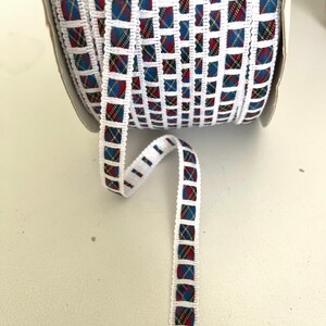May include: White ribbon with a blue, red, and yellow plaid pattern. The ribbon is trimmed with white and has a square design.