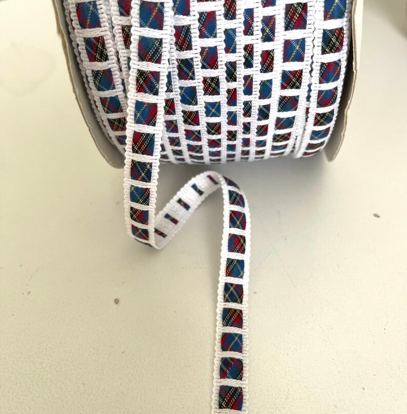 May include: White ribbon with a blue, red, and yellow plaid pattern. The ribbon is trimmed with white and has a square design.