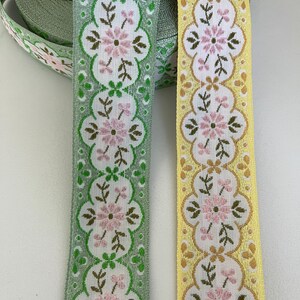 May include: Two floral patterned ribbon trims, one in green and one in yellow. Both trims feature a repeating pattern of pink flowers and green leaves.