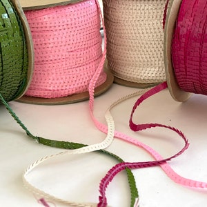 May include: Four spools of sequined trim in green, pink, cream, and burgundy. The trim is made of small square sequins sewn together in a continuous line.