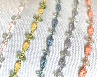 May include: Five different colored crocheted trims with a leaf and flower design. The trims are pink, yellow, blue, purple, and peach.