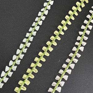 May include: Three rows of green and white trim with a scalloped edge. The trim is made of a woven fabric and has a delicate, feminine look.