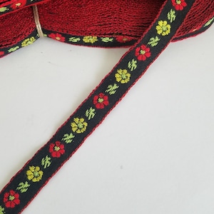 May include: Red and black woven ribbon with a floral pattern. The ribbon has a black background with red and yellow flowers. The ribbon is rolled up and tied with twine.