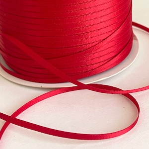 May include: A spool of bright red satin ribbon. The ribbon is wound tightly on the spool and is ready to be used for crafting, decorating, or gift wrapping.