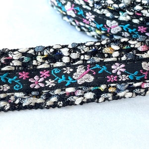 May include: Black and white trim with a colorful floral design. The trim features pink, blue, and white flowers with green leaves. The trim is textured and has a slightly raised design.