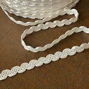 May include: White crocheted trim with a scalloped edge. The trim is shown in a close-up view.