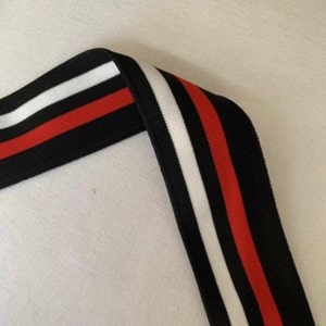 May include: Black and white striped trim with red stripes. The trim is made of a soft, stretchy fabric.