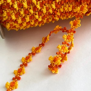 Könnte beinhalten: Eine Spule mit gelbem und orangefarbenem Besatz mit einem gekräuselten Rand. Der Besatz ist aus einem weichen, gewebten Stoff gefertigt und hat ein zartes, florales Muster.