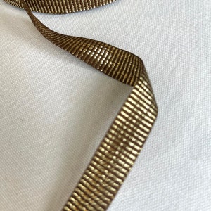 May include: Brown ribbon with a gold metallic stripe. The ribbon is woven with a subtle texture.