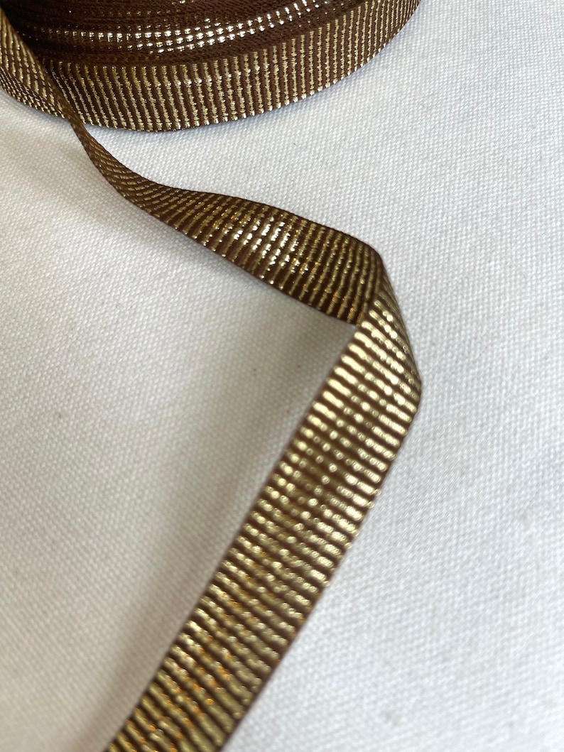 May include: Brown ribbon with a gold metallic stripe. The ribbon is woven with a subtle texture.