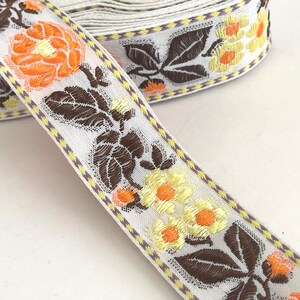 May include: White fabric ribbon with a brown, yellow, and orange floral pattern. The ribbon has a checkered border.