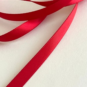 May include: Red satin ribbon, a thin, smooth, and shiny ribbon with a subtle sheen.