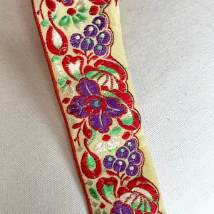 May include: A close-up of a yellow fabric trim with a floral design. The trim features red, green, purple, and white embroidery. The trim is perfect for adding a touch of elegance to any project.