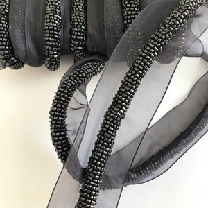 May include: Black beaded trim ribbon with a sheer black fabric backing. The ribbon is made of small black beads sewn together in a continuous line.