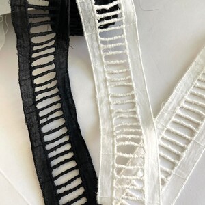 May include: Close-up of two decorative ribbons. One is black, the other is white. Both ribbons have a cut-out design with rectangular openings. The ribbons are made of a woven fabric and are likely used for crafting or embellishment.