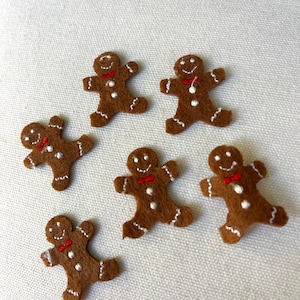 May include: Six brown felt gingerbread man ornaments with white icing details and red bow ties.